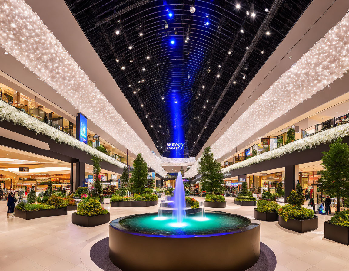 Mall interior with central fountain, greenery, shops, and illuminated ceiling