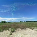 Desert landscape with green dunes, patterned sky, stones, and white dome