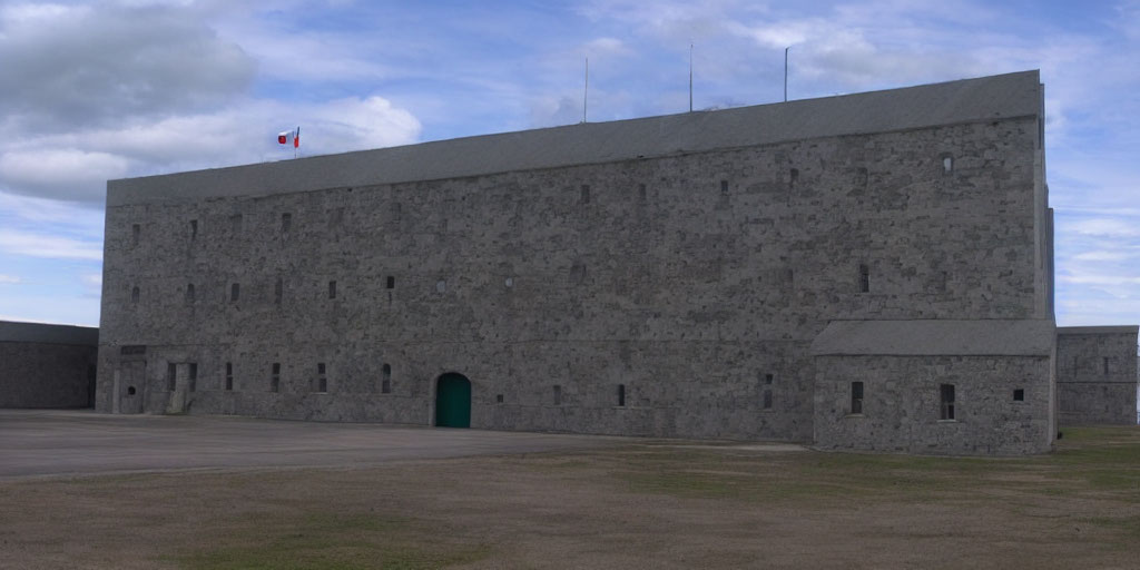 Gray stone fortress with flag and arched green door under cloudy sky