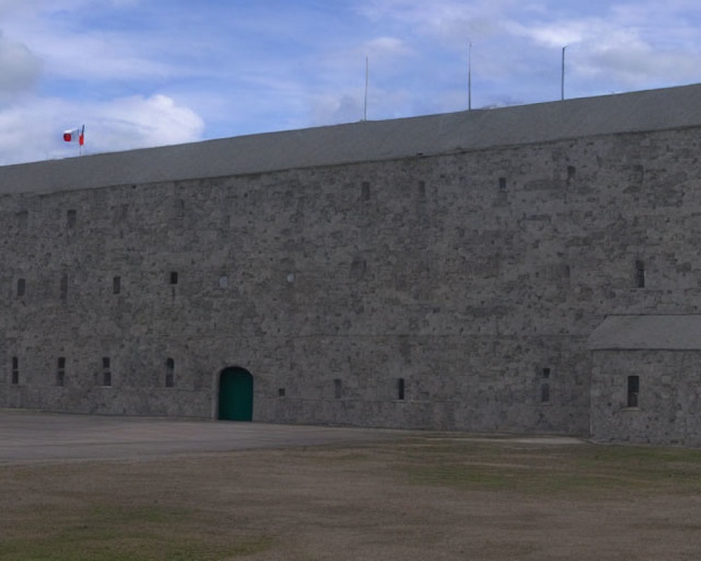 Gray stone fortress with flag and arched green door under cloudy sky