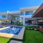 Spacious two-story house with large windows, white exterior, pool, and manicured lawn