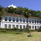 Two-story colonial white building with brown shutters, palm trees, and green lawn under a blue sky