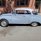 Vintage luxury car parked with man in suit and classic cars in background