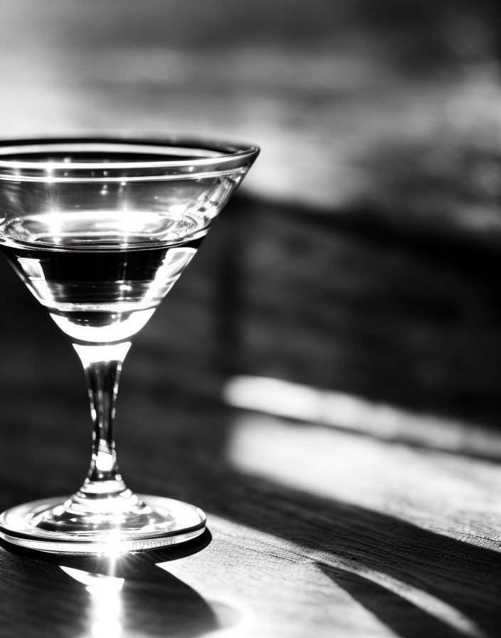 Monochrome martini glass on wooden surface with shadow