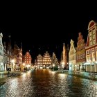 Medieval town square at night with illuminated market stalls and timber-framed buildings.