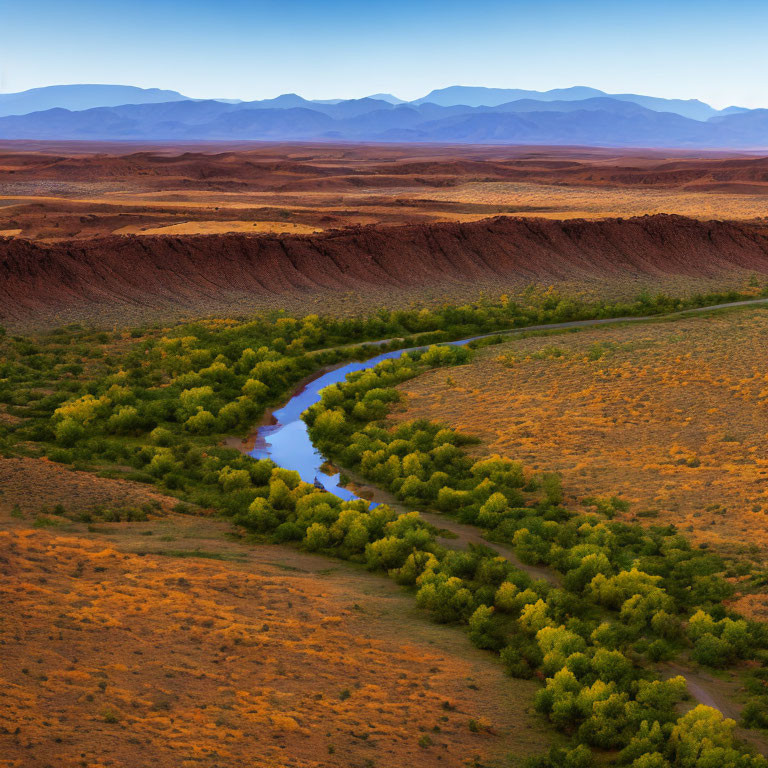 Serpentine river winding through dry landscape with orange soil and green shrubbery against layered mountain ranges