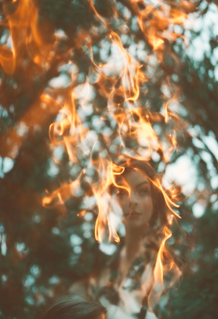 Woman's face obscured by dancing flames against blurred greenery