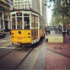 Vintage yellow streetcar on rain-slicked tracks in bustling city avenue at dusk