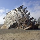 Sunlit wrecked ship on sandy shore with damaged hull and tattered sails.