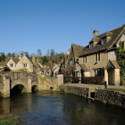 Medieval village with stone buildings, stream, old bridge, and mist at twilight