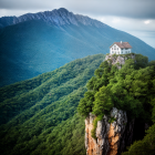 Charming cottage on grassy cliff with rock formations and trees under cloudy sky