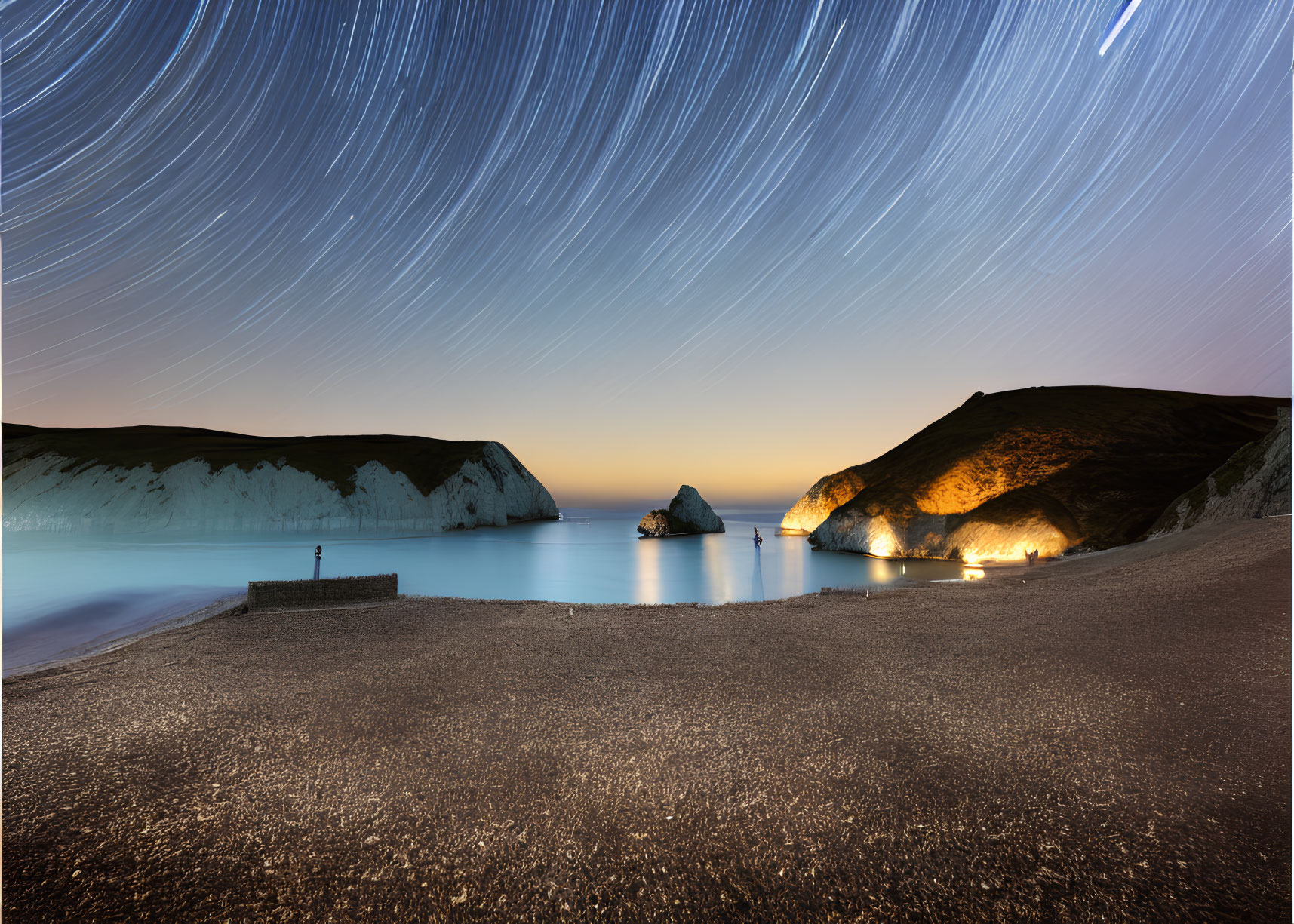 Nighttime Coastal Scene: Star Trails, White Cliffs, Lit Beachfront