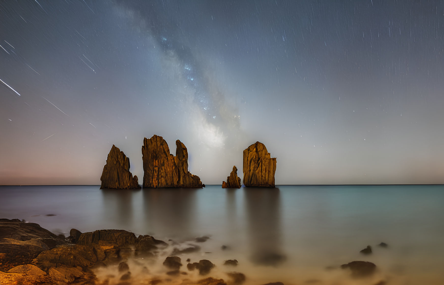 Starry night seascape with Milky Way and rock formations in calm ocean