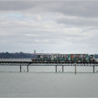 Blue train crossing pier over calm waters under dramatic cloudy sky