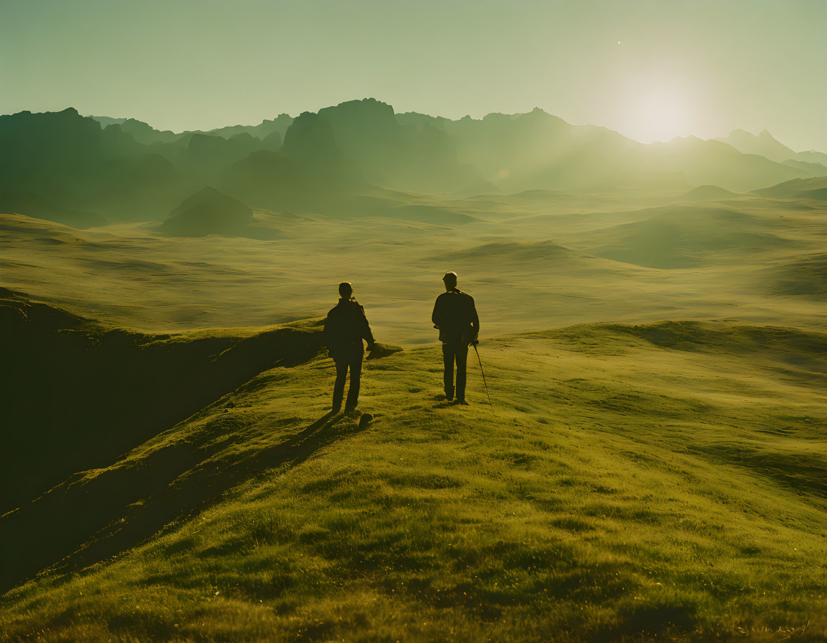 Hikers on grassy hill at sunset with mountains in background