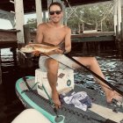 Person with sunglasses holds fish on boat with fishing gear on sunny day