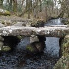 Snow-covered stone bridge, bare trees, tranquil river in serene winter scene