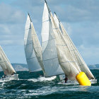 Sailboats racing tightly around yellow buoy on choppy ocean waters