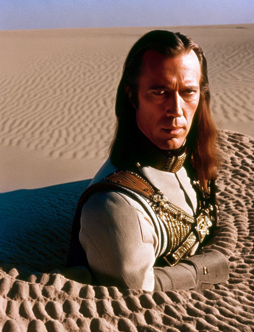 Man in Long Hair in Military-Style Uniform Kneeling in Desert