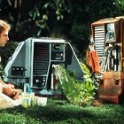 Lab-coated individual operates vintage computer equipment with multiple monitors.