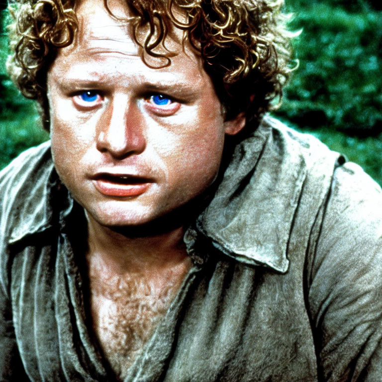 Close-up portrait of person with curly hair, bright blue eyes, and concerned expression in green shirt