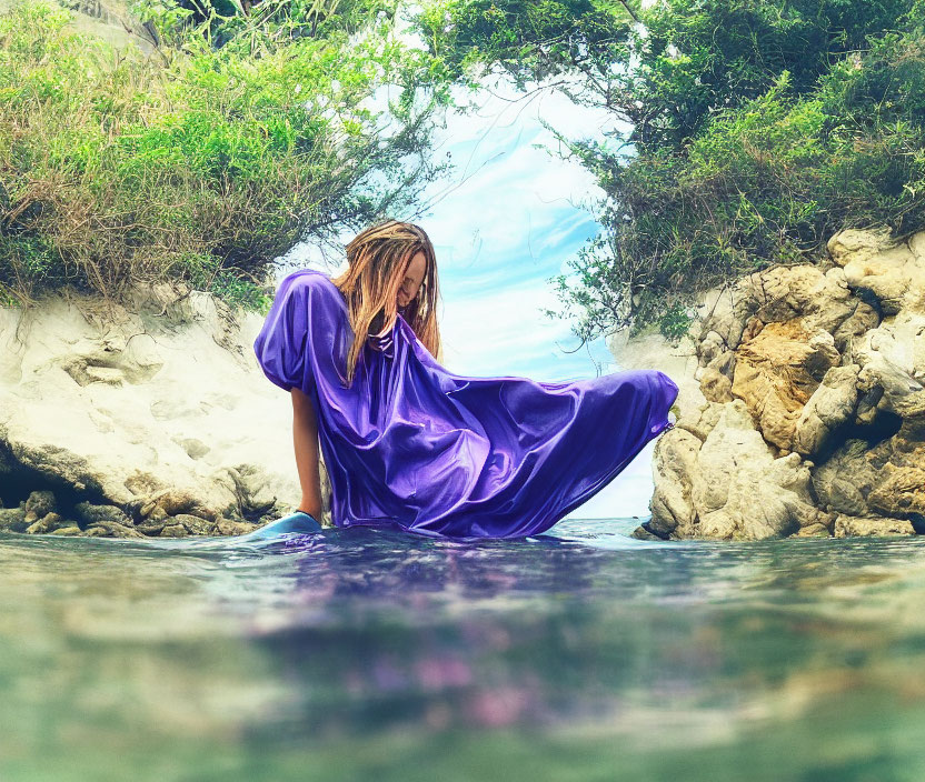 Person in Purple Gown Sitting in Shallow Water with Mossy Rocks