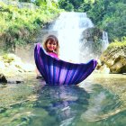 Person in Purple Gown Sitting in Shallow Water with Mossy Rocks