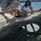 Dark-haired mermaid on rock by sea with glistening tail and crashing waves