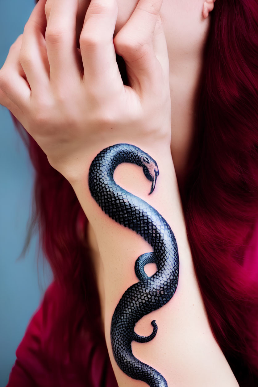 Red-haired person displaying realistic snake tattoo on forearm against blue background