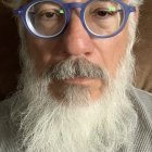 Elderly man with white beard and glasses in patterned shirt