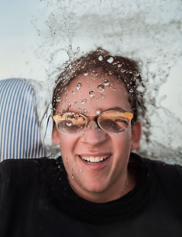 Smiling person behind clear water splash with suspended droplets and eyeglasses