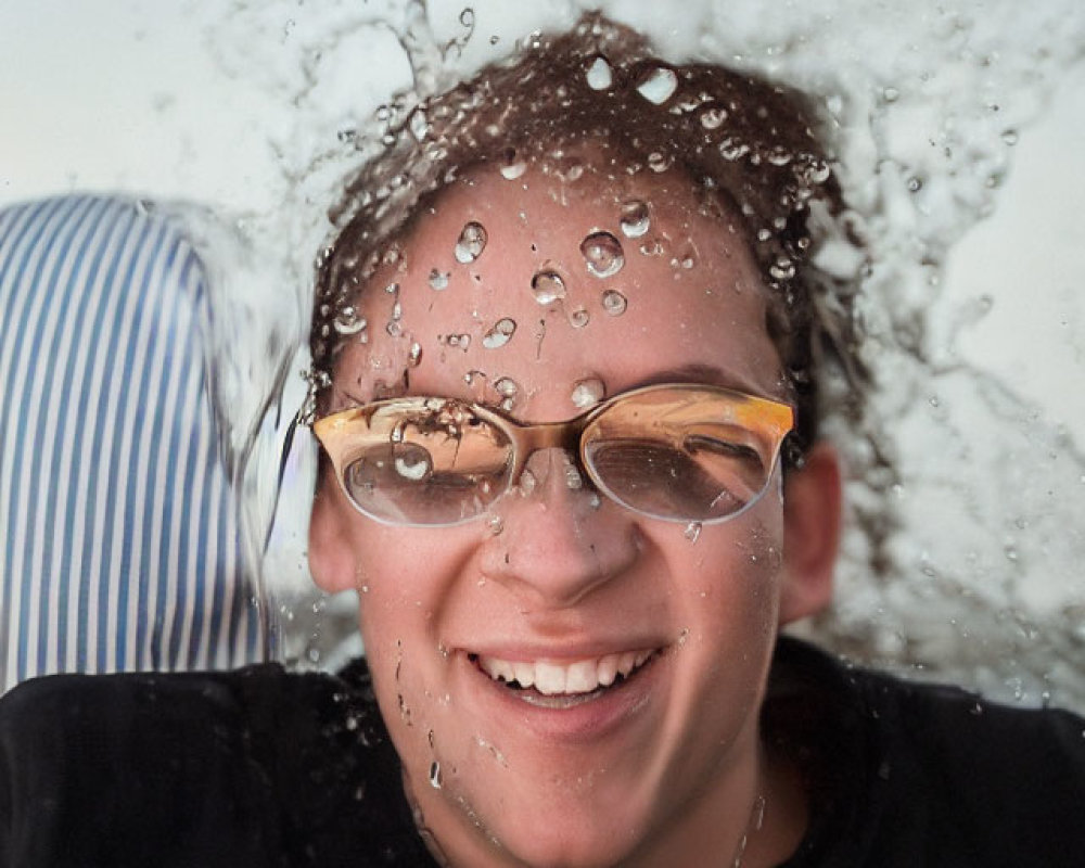 Smiling person behind clear water splash with suspended droplets and eyeglasses