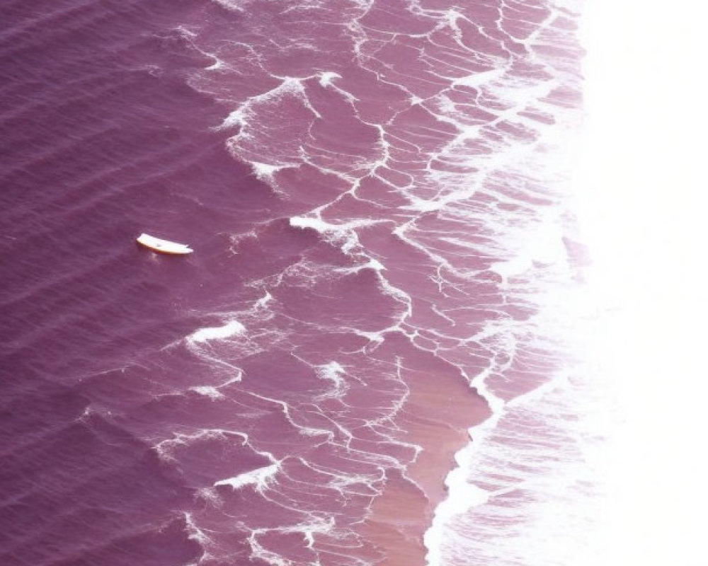 Pink-hued shore with white waves and boat in aerial view