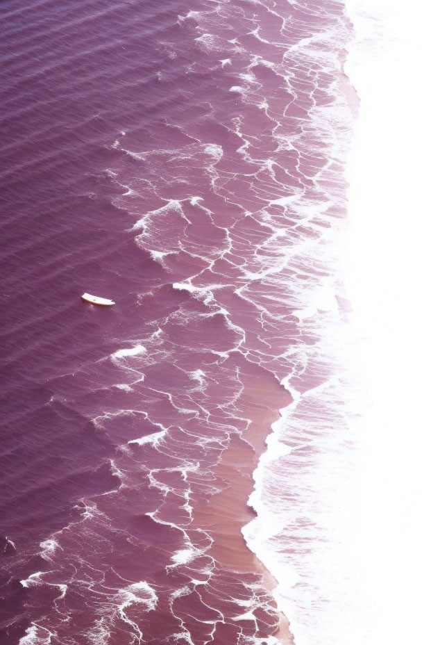 Pink-hued shore with white waves and boat in aerial view