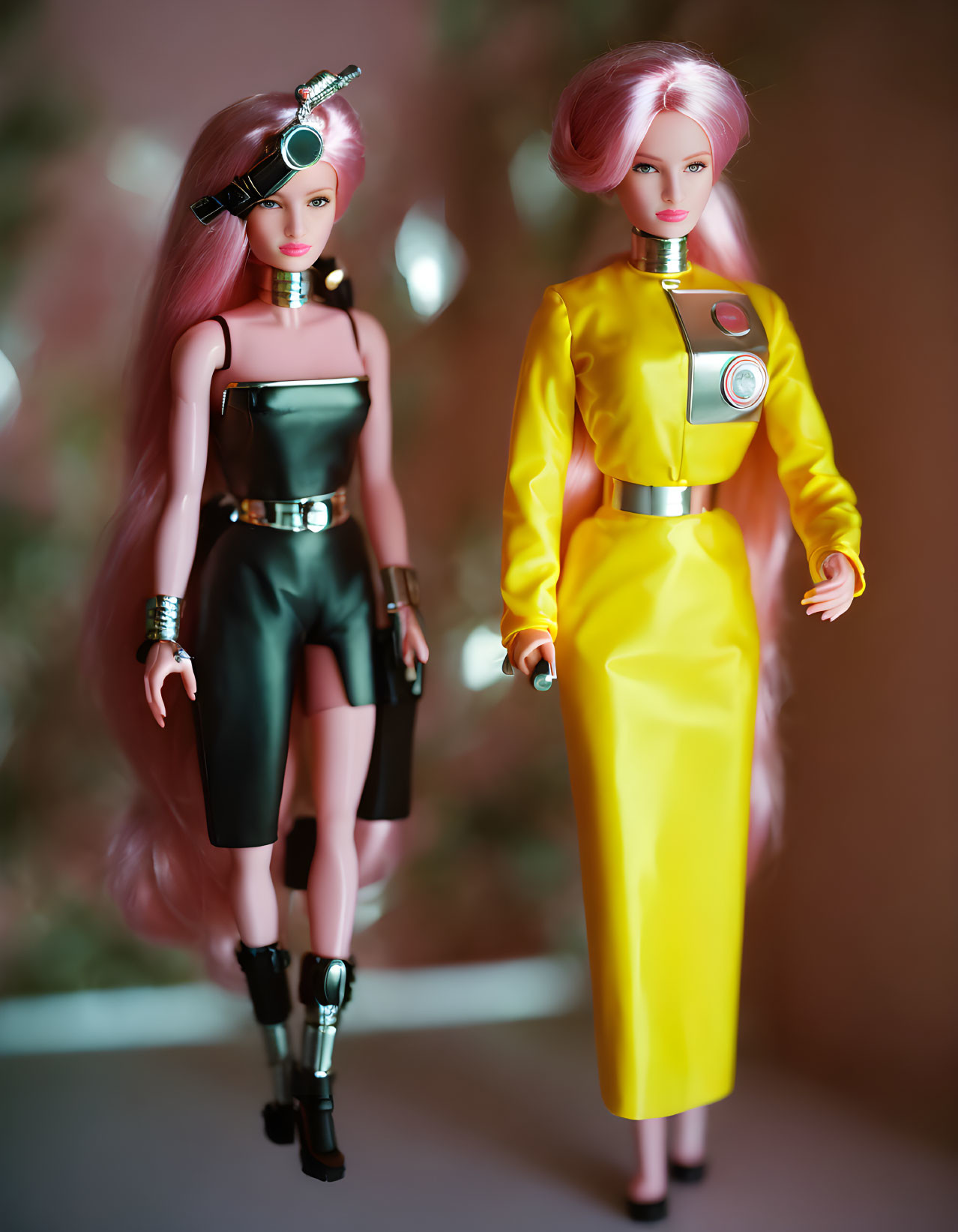 Fashion dolls in futuristic black and silver outfit with eye patch, and yellow dress with circular chest device.