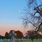 Mythical cemetery with glowing full moon, cross gravestone, fireflies, red foliage trees,
