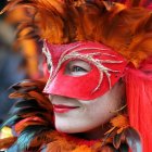 Person in Red and Silver Mask with Feathered Headdress on Dark Background