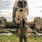 Person in Red Headscarf Surrounded by Derelict Planes and Cars