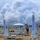 Scenic beach with umbrellas, lighthouse, sailboats, and cloudy sky