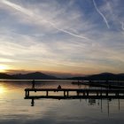 Tranquil sunrise scene with sailing ships, rowboat, and mountains.