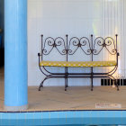 Metal bench with yellow cushions against blue curtains and tiled flooring by a pool