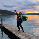 Woman dancing on wooden pier at sunset with mountain lake landscape