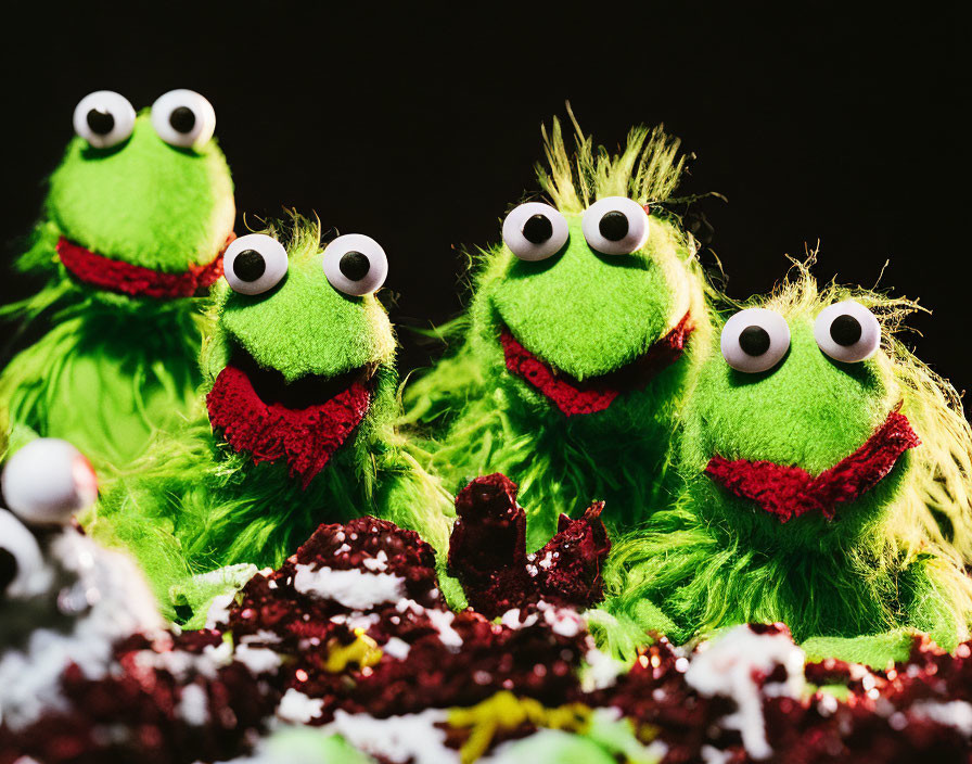 Four green furry toy monsters with large eyes and red mouths on dark background