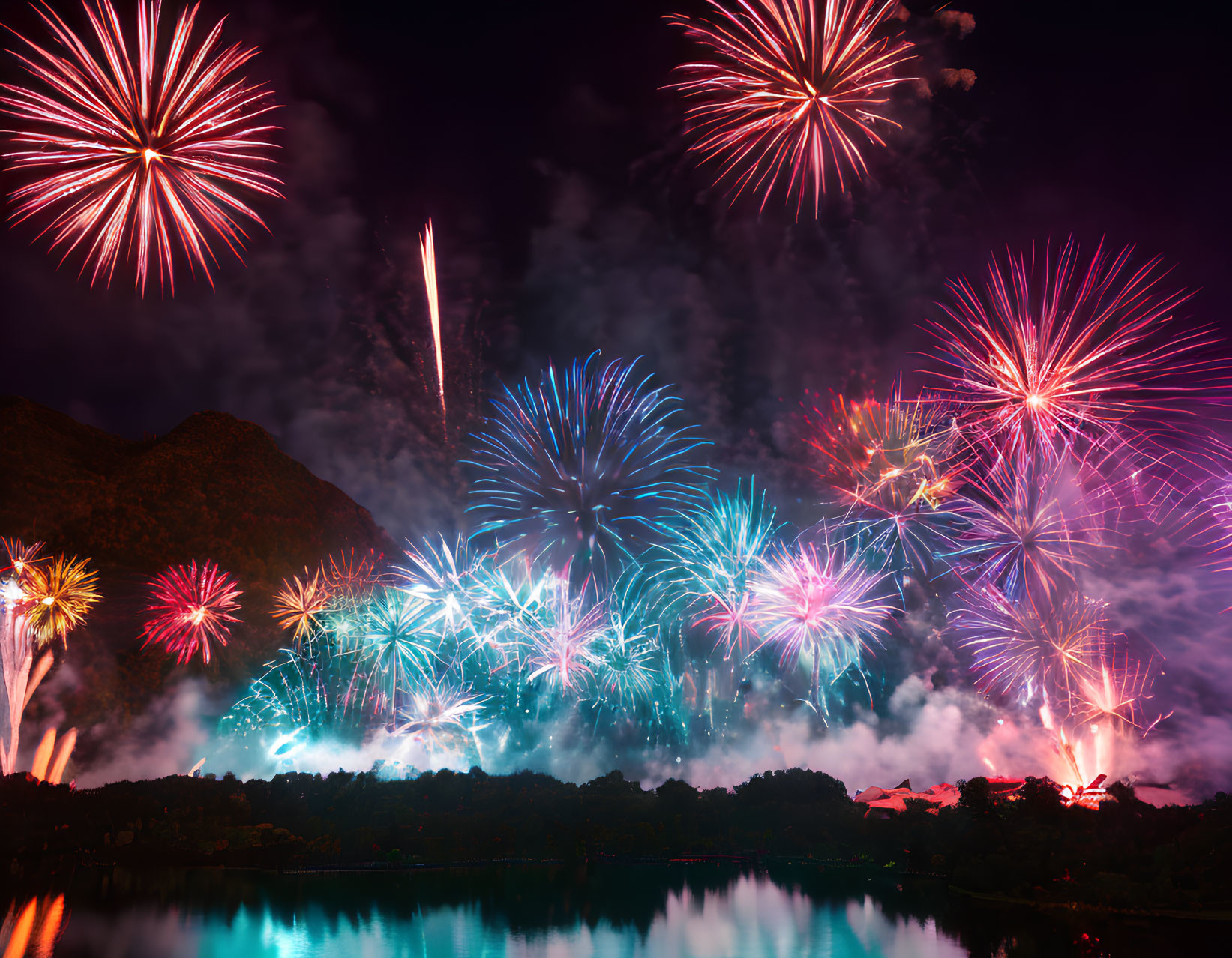 Colorful fireworks illuminate lake with tree silhouettes and mountains at night