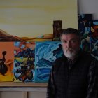 Grey-bearded man contemplates abstract paintings in artist's studio