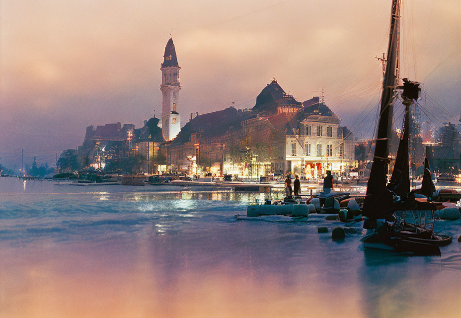 Cityscape with illuminated buildings, clock tower, and sailboat at twilight