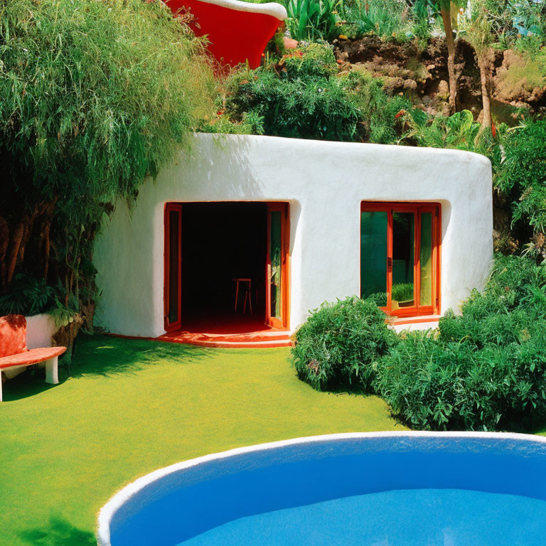 White Rounded House with Bright Orange Accents in Lush Greenery Next to Blue Pool