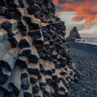 Patterned rock formations and arch-shaped rock with crashing wave in surreal coastal landscape.