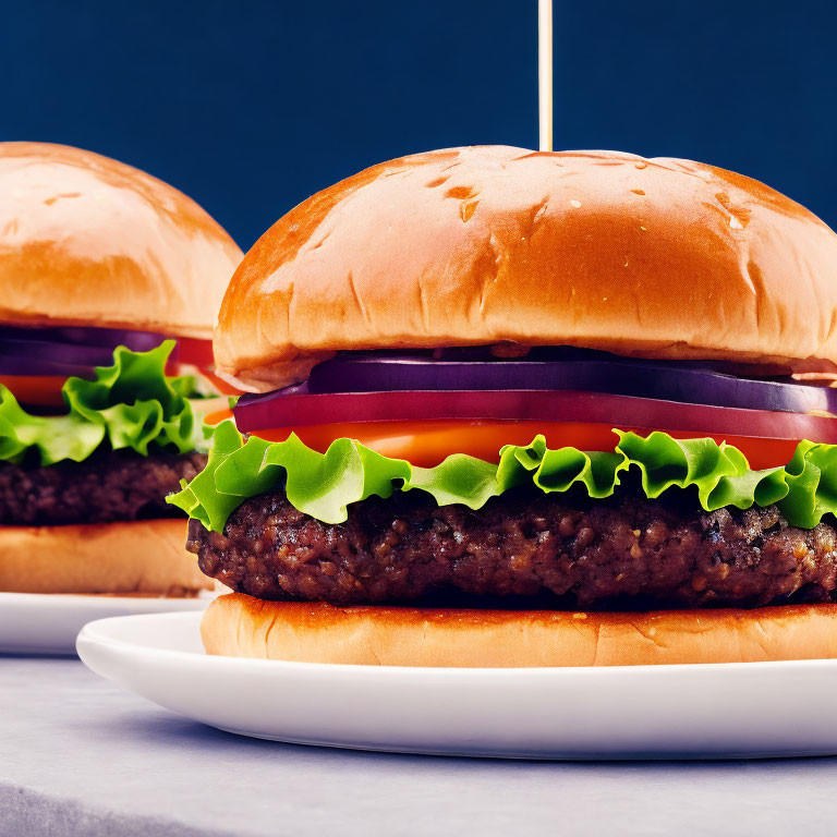 Two cheeseburgers on brioche buns with lettuce, tomatoes, onions on white plates