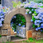 Stone cottage with white gate and vibrant flowering bushes under clear blue sky